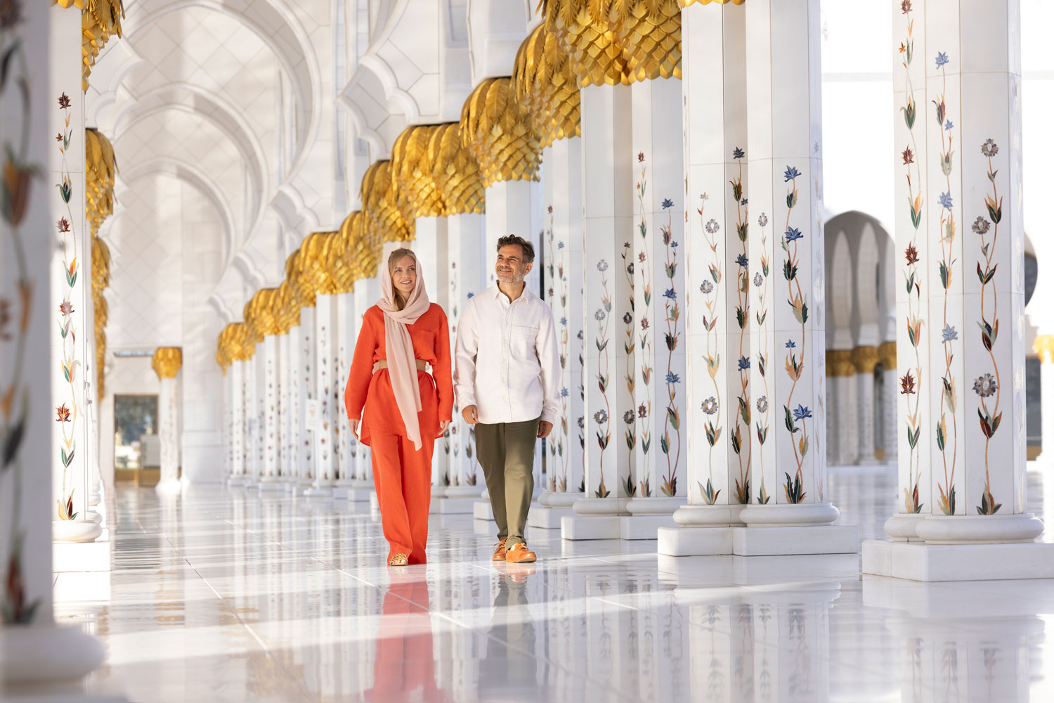 Couple walking through the elegant Sheikh Zayed Grand Mosque with stunning marble columns.