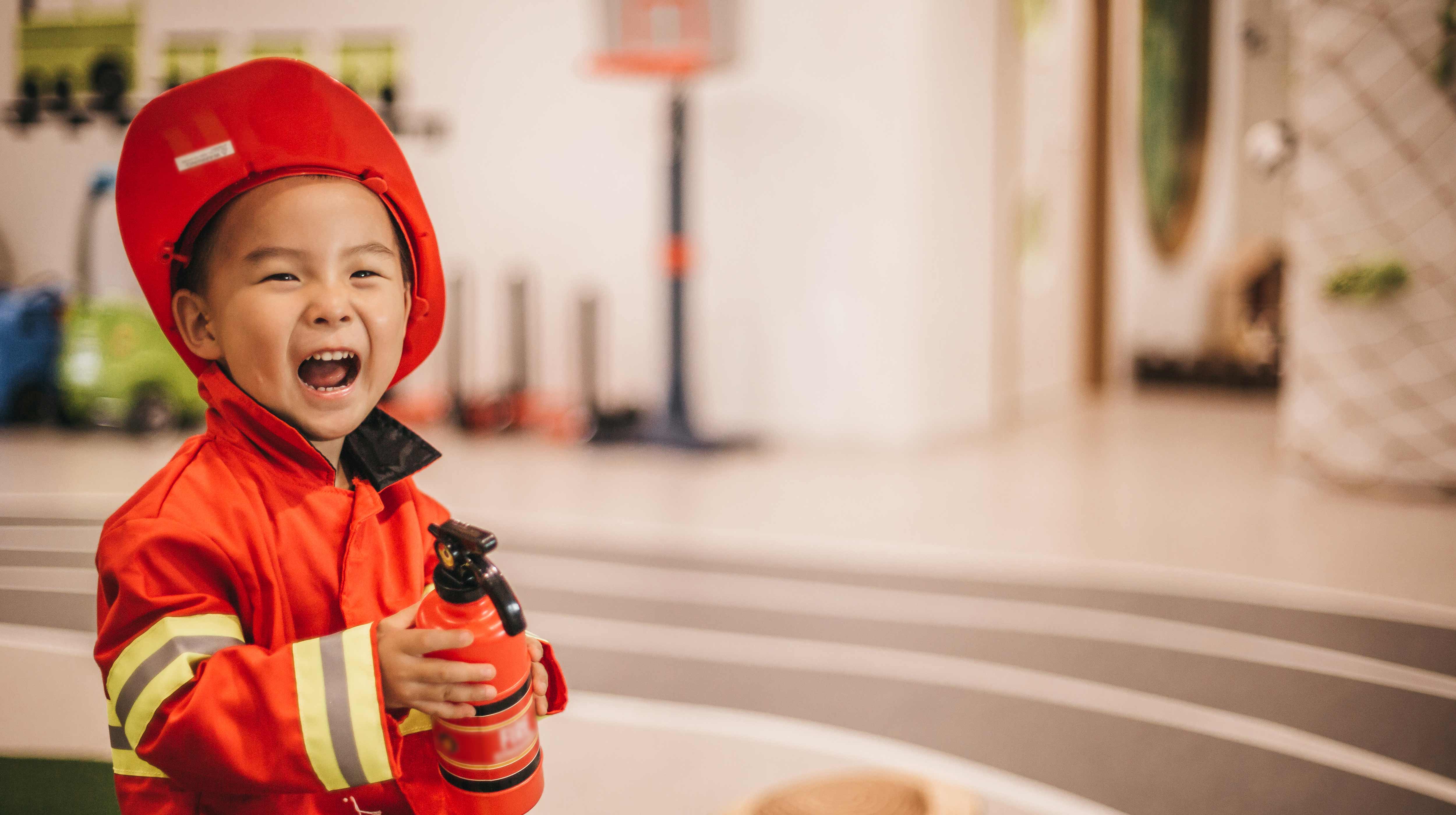 Un bambino vestito da pompiere ride felice con un mini estintore mentre gioca nella mini città dedicata ai bambini KidZania ad Abu Dhabi