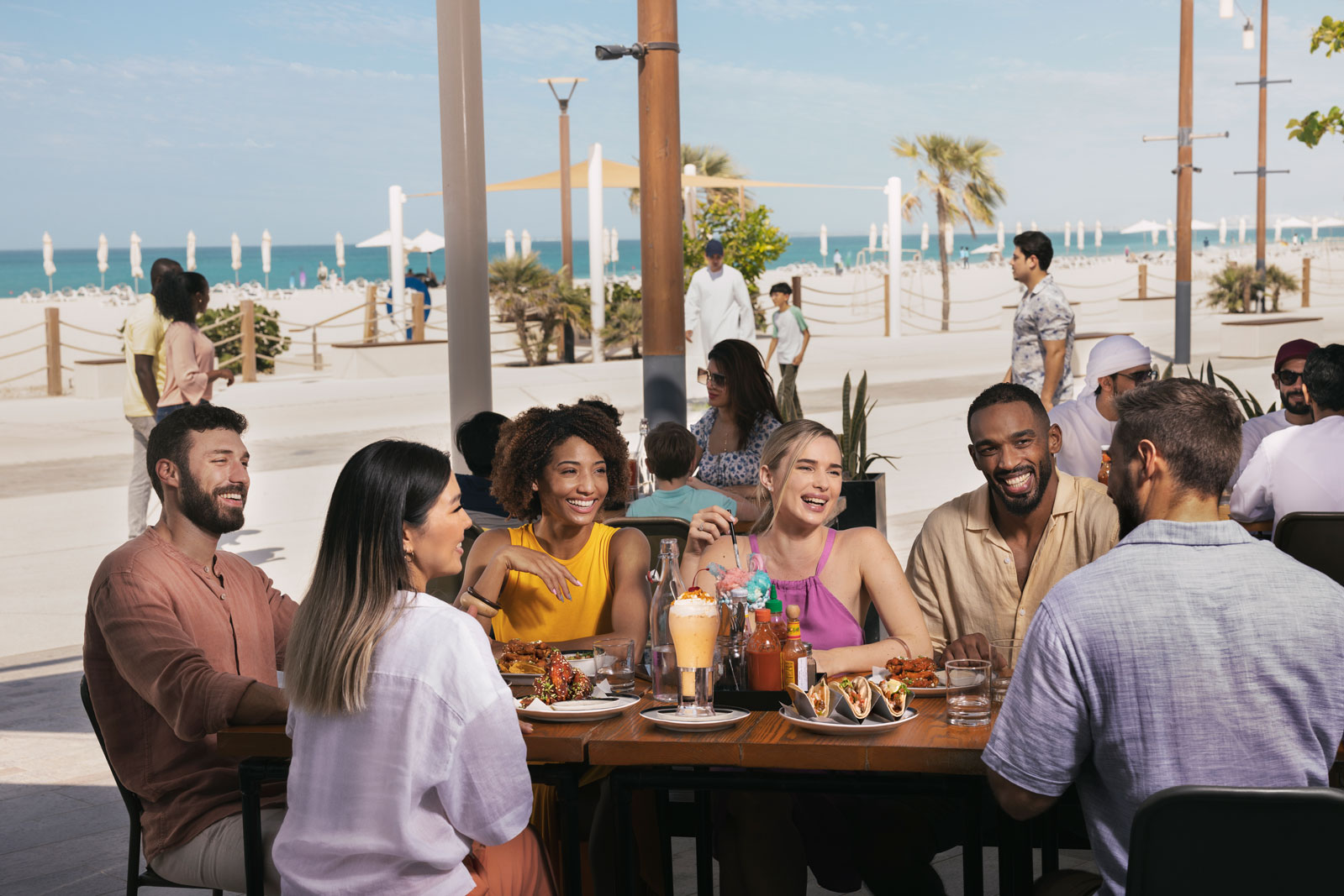 Group of friends enjoying food and drinks at a beachside restaurant in Abu Dhabi with ocean views.
