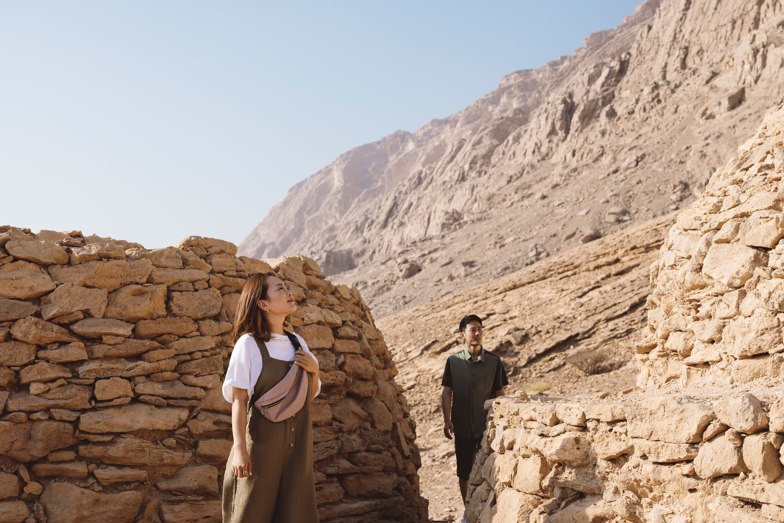 Explorers walking through the ancient stone ruins of the Hili Archaeological Park area in Al Ain, surrounded by rugged Jebel Hafeet mountain terrain.