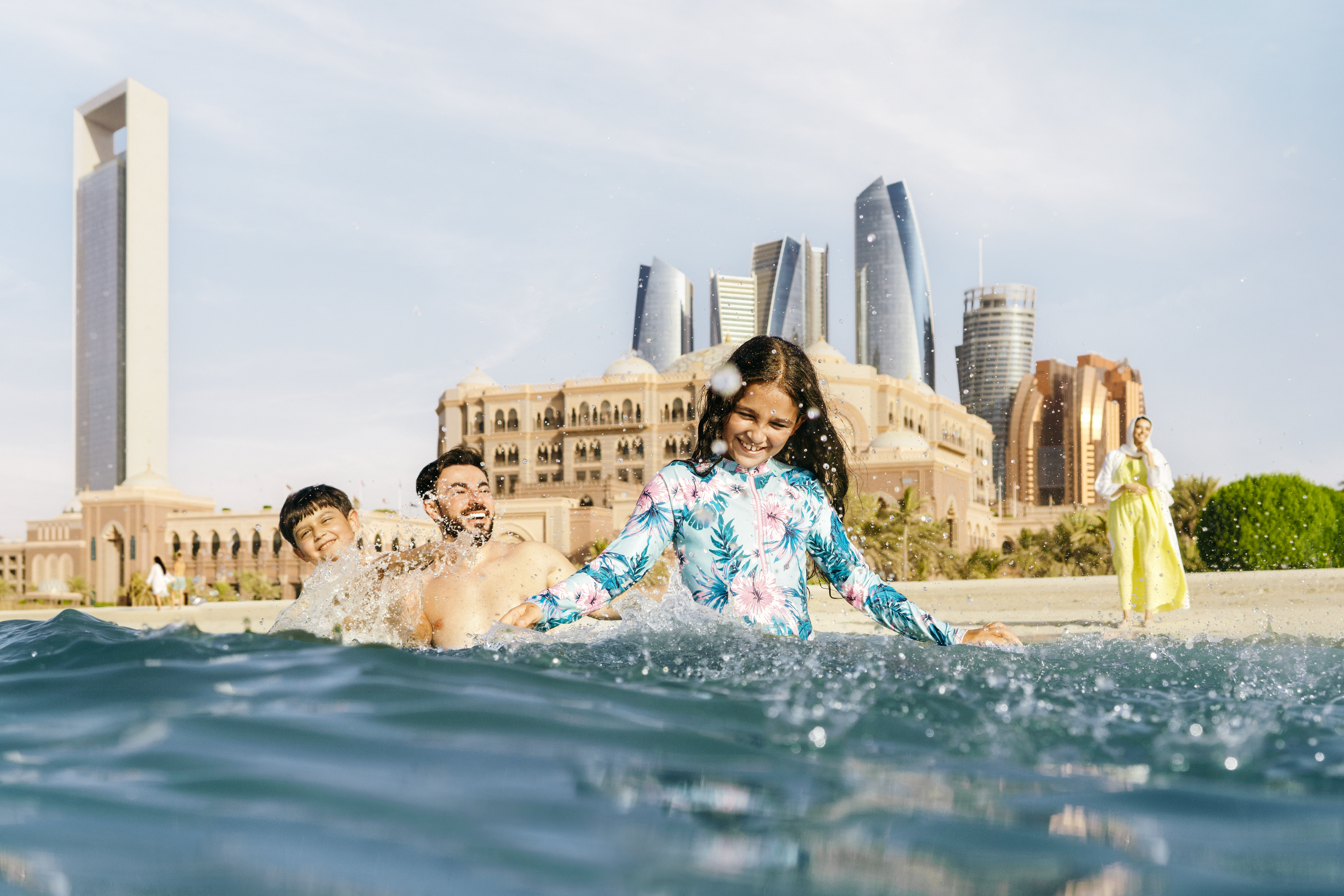 Famiglia che si diverte in acqua sotto il sole di Abu Dhabi con l'Emirates Palace e i grattacieli sullo sfondo