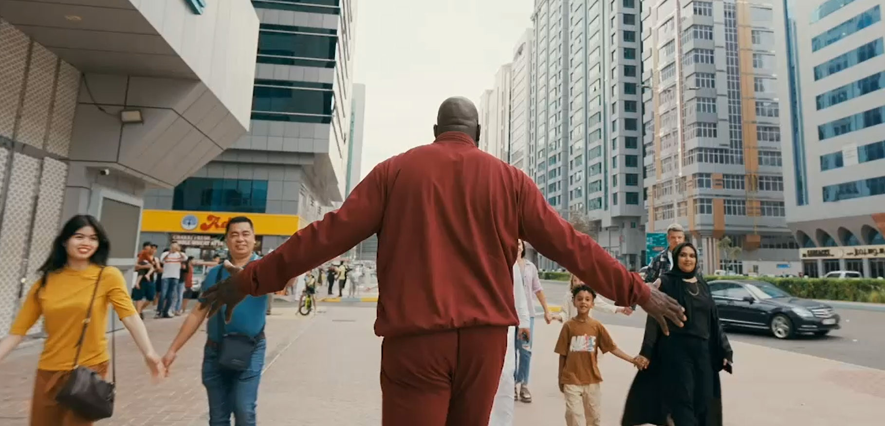 Diverse group holding hands in a city street led by man in red tracksuit, Abu Dhabi.