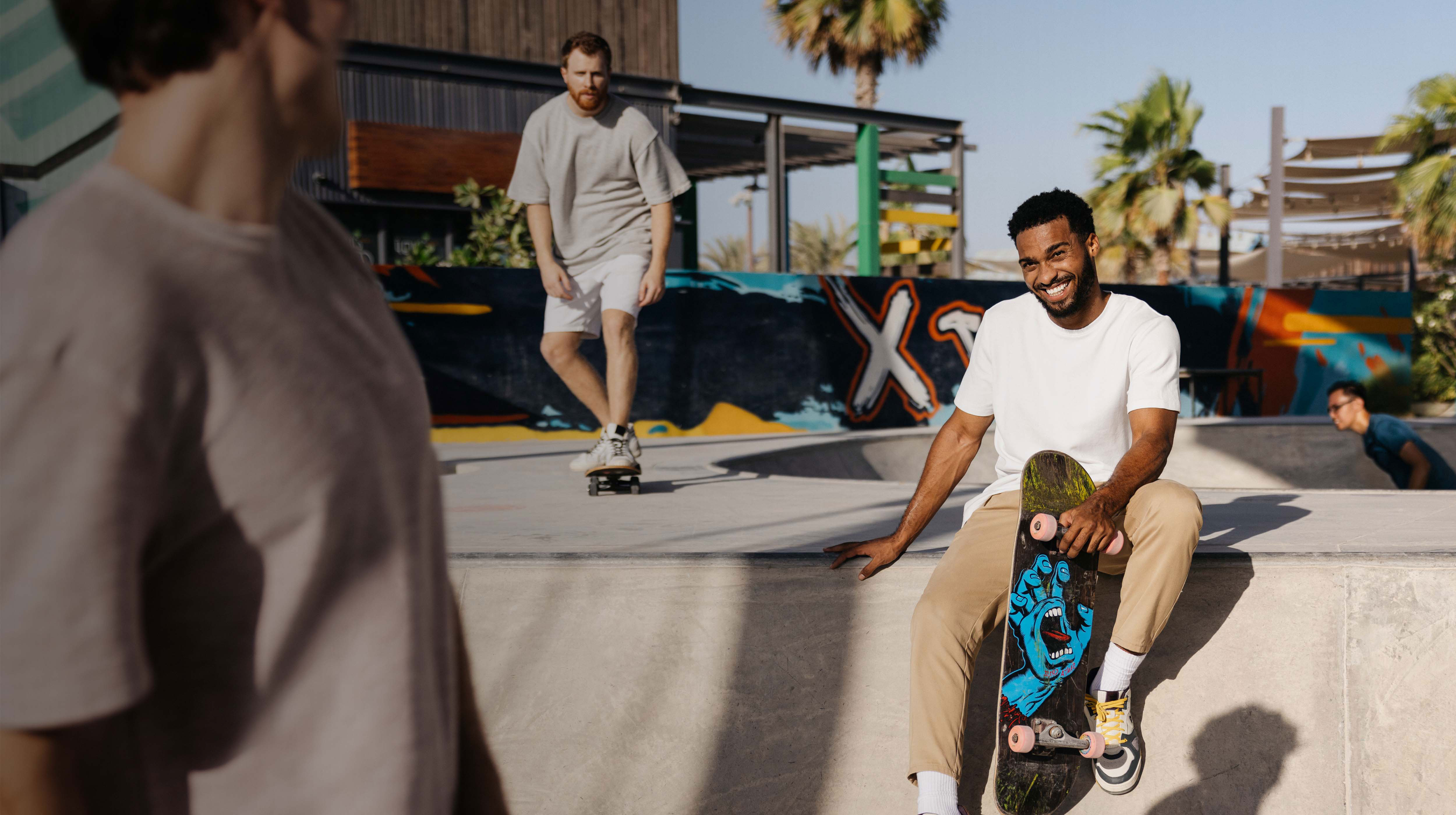 Group of friends enjoying a sunny afternoon at a skatepark in Abu Dhabi’s Hudayriyat Island, with vibrant graffiti, palm trees, and laid-back energy all around.