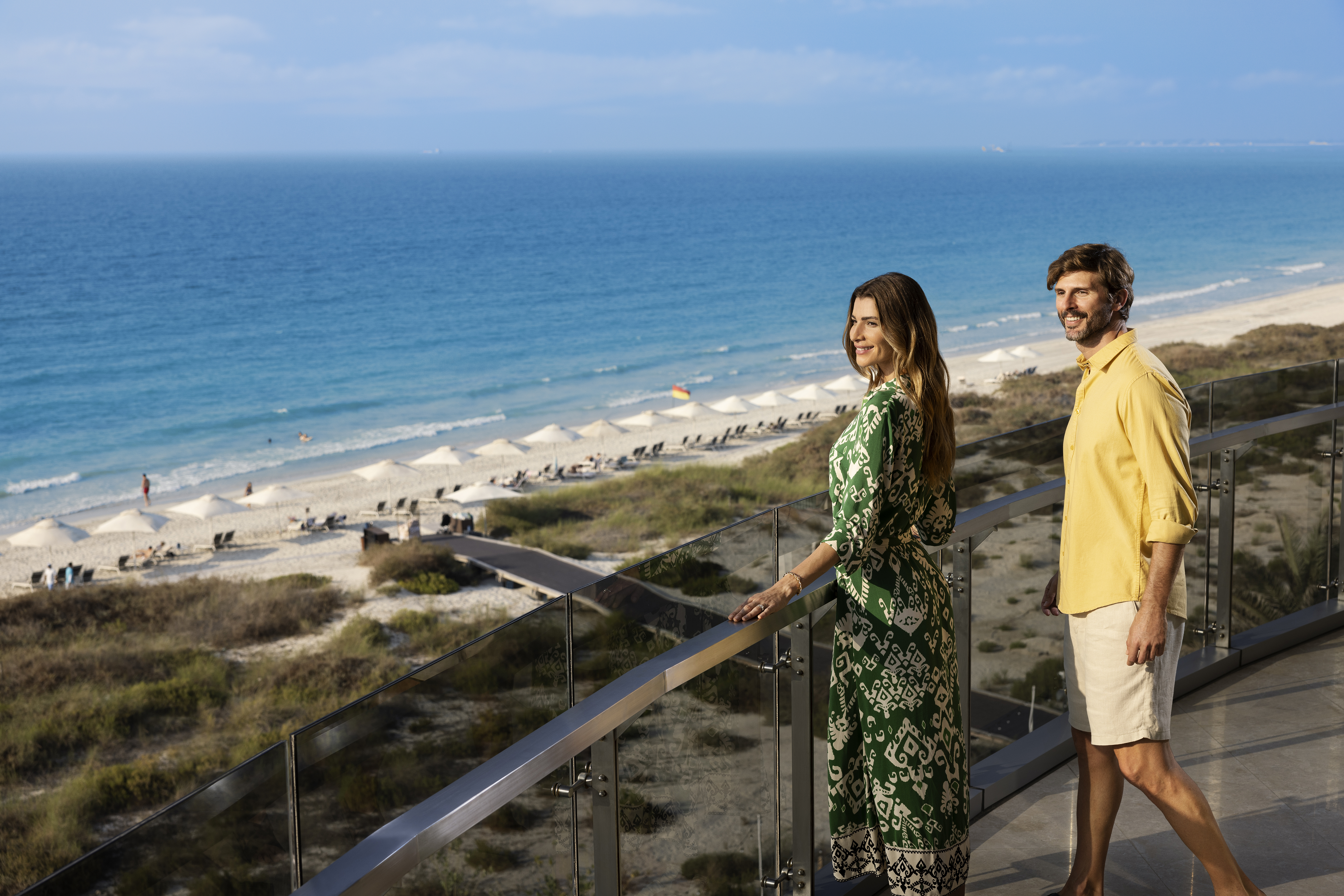 Couple enjoying a serene view of Abu Dhabi’s pristine Jumeirah beach from a luxury resort balcony.