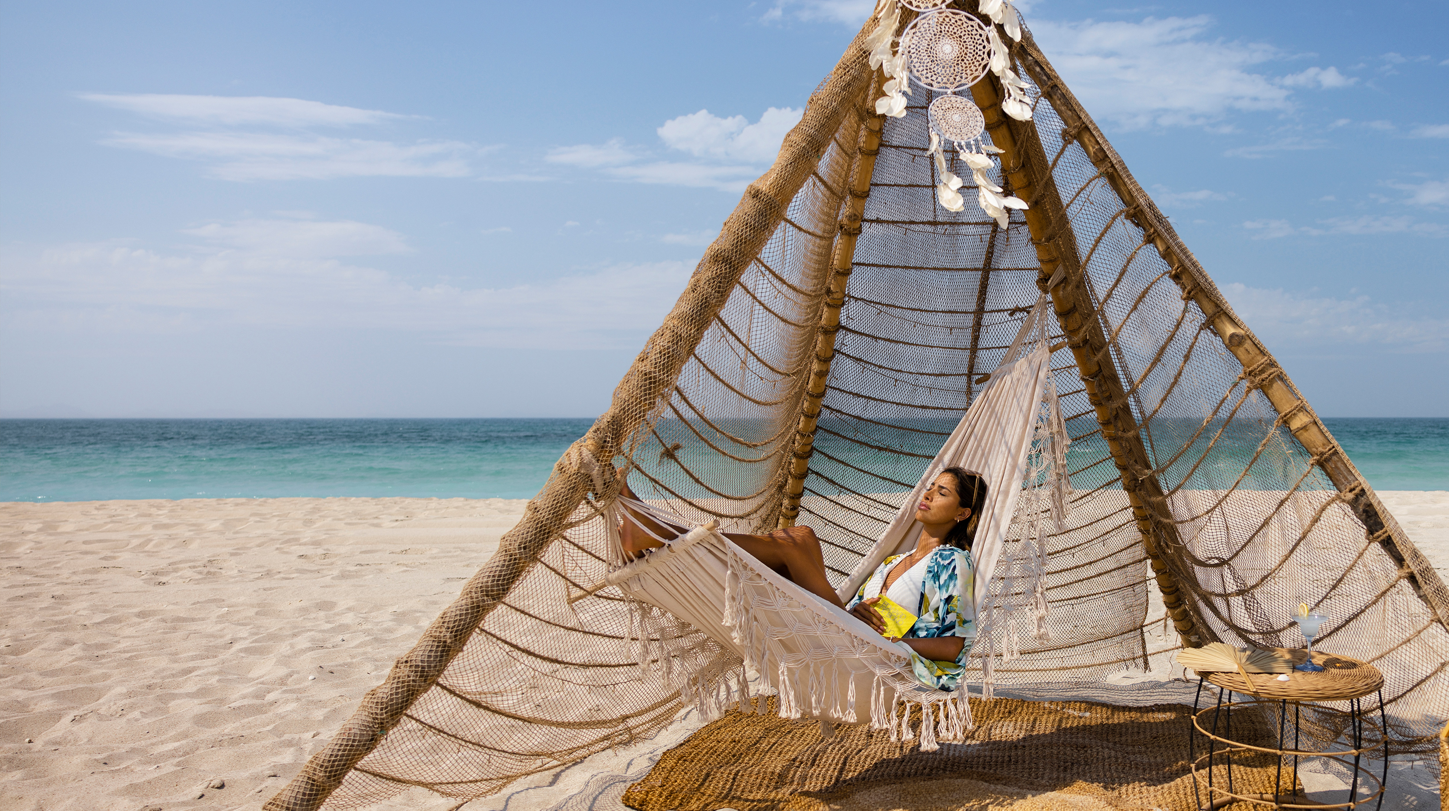 Woman relaxing on a hammock under a beach canopy with ocean views and sunny skies in Abu Dhabi