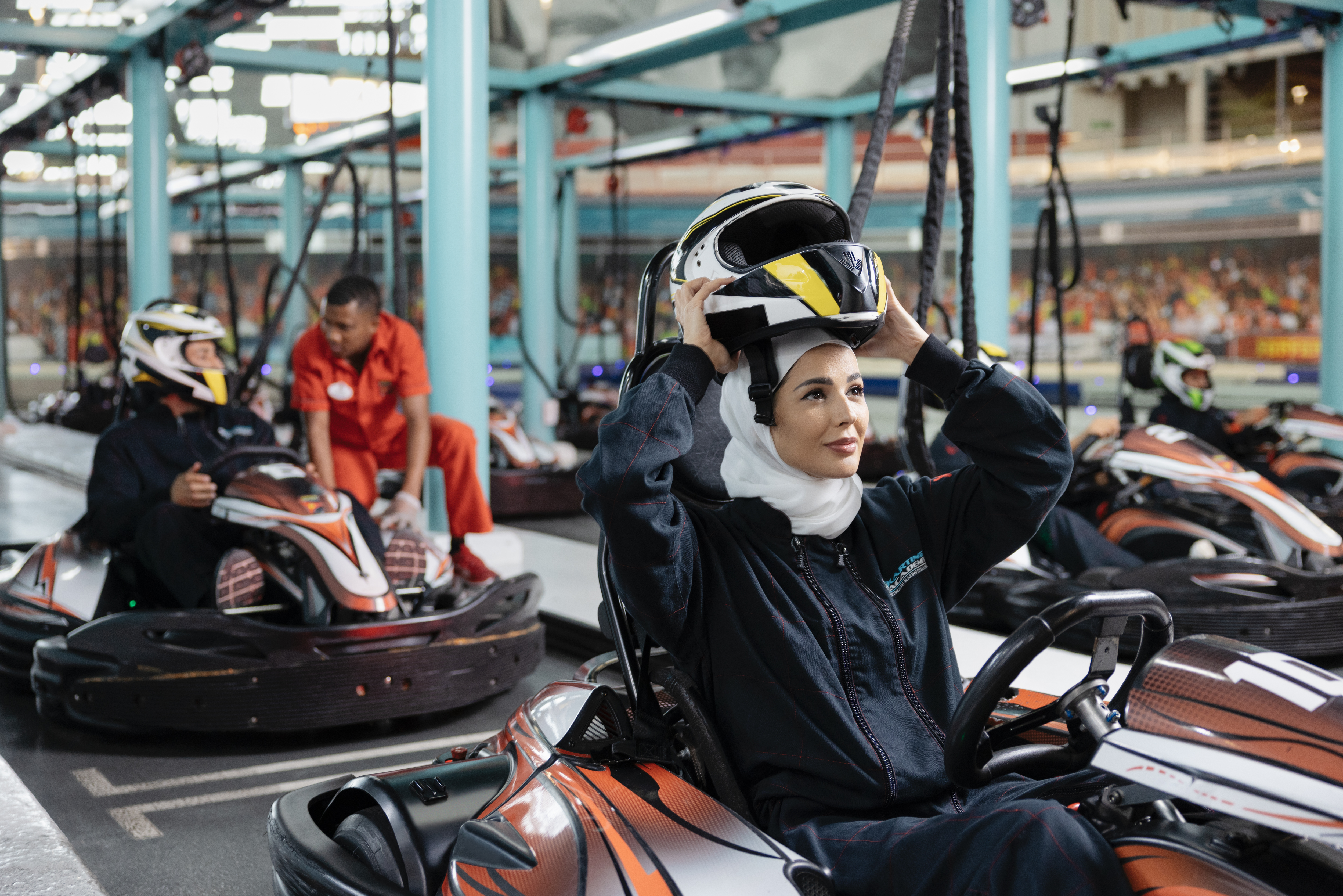 Woman in racing suit preparing for indoor go-karting at a vibrant track in Abu Dhabi with others