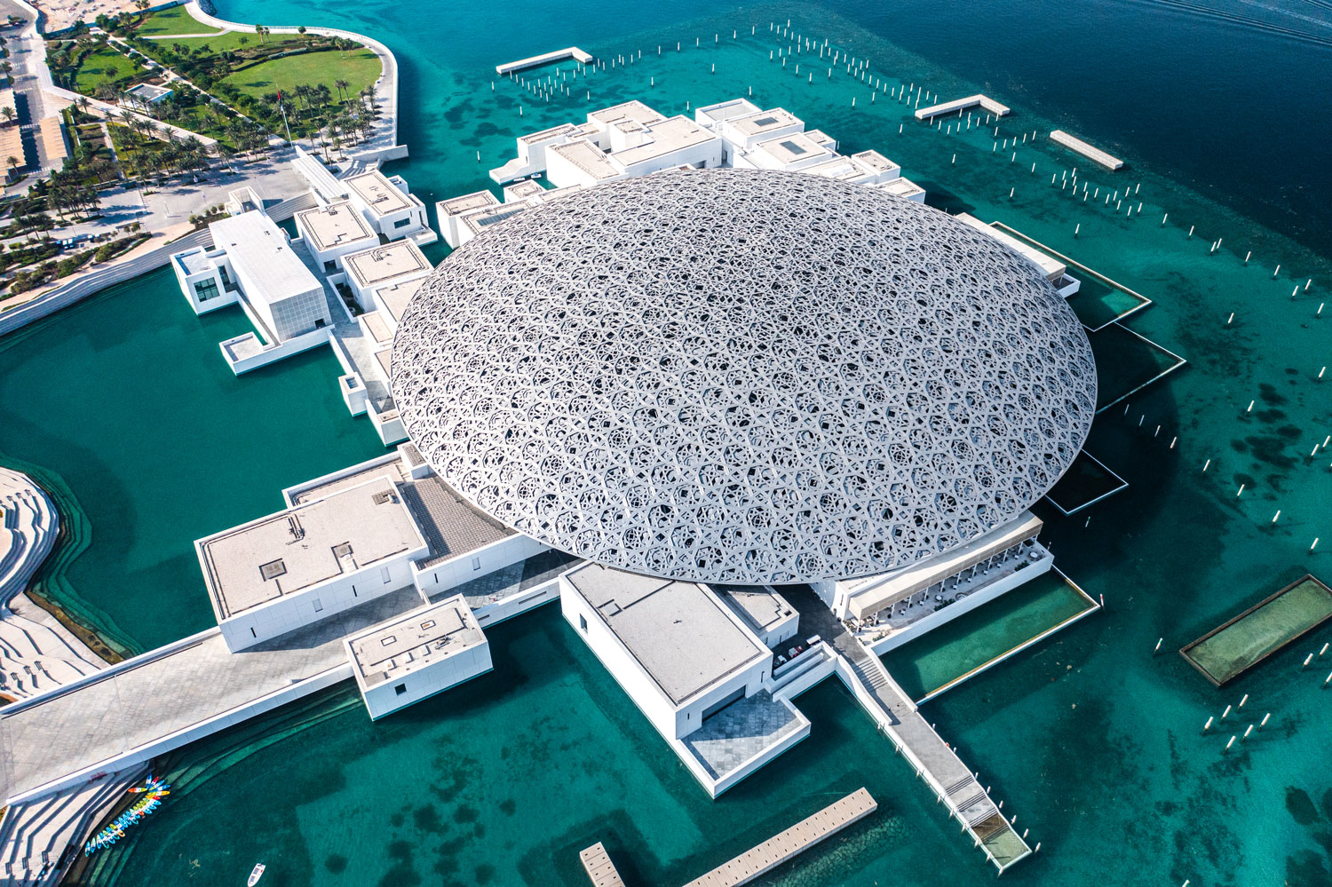 Close-up aerial view of Louvre Abu Dhabi's intricate dome surrounded by turquoise waters and walkways