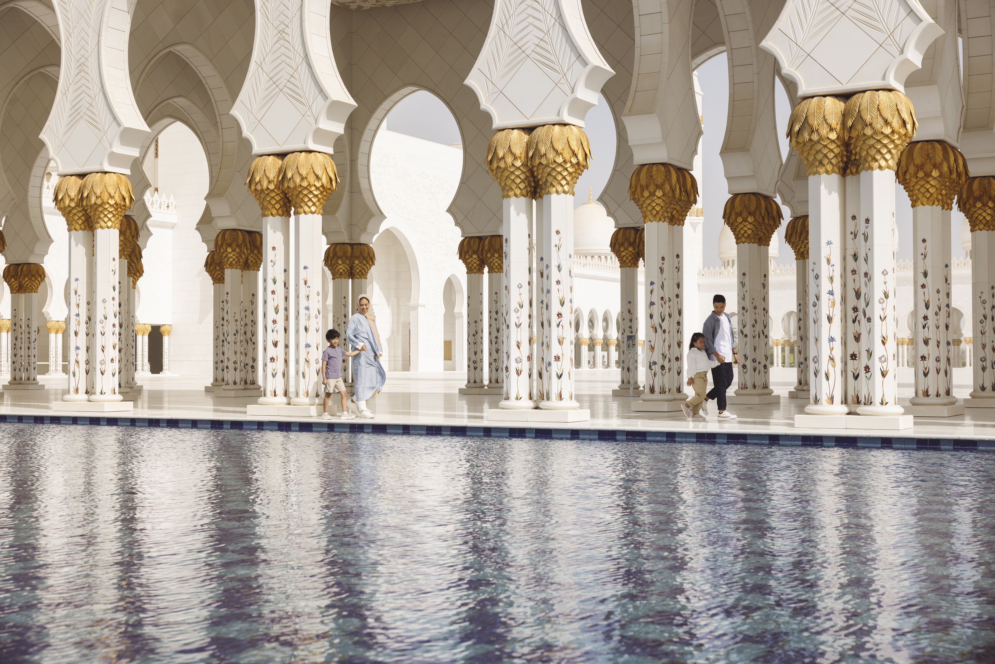 Famiglia che cammina tra le colonne decorate della Grande Moschea dello Sceicco Zayed ad Abu Dhabi.